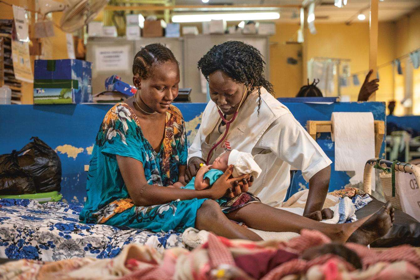 An MSF nurse and patient sit on a hospital bed with a newborn baby in Aweil, South Sudan.